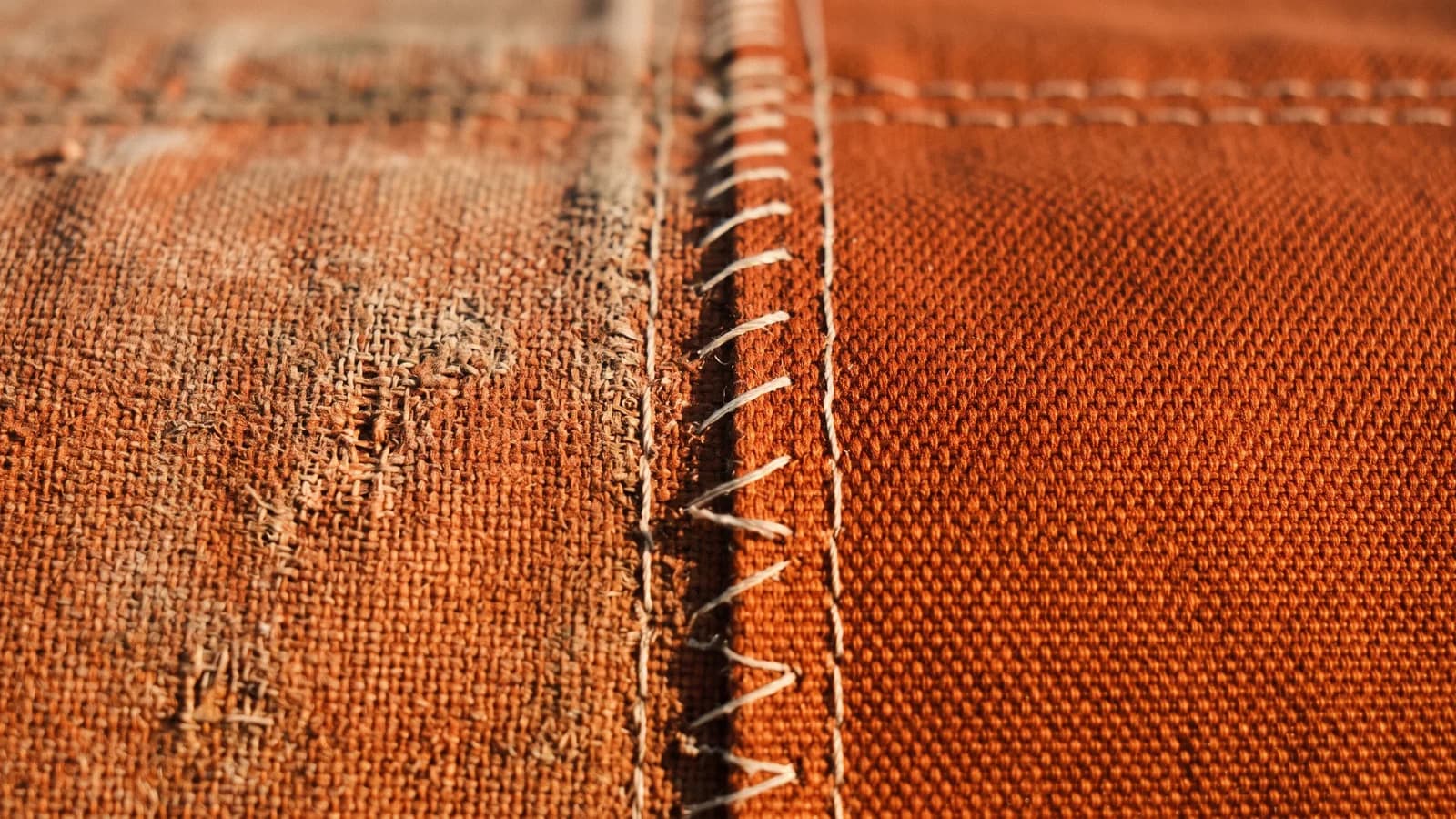 Close view of awning fabric at the seam where a sun faded panel meets a newer replacement panel, weave visible in raking light.